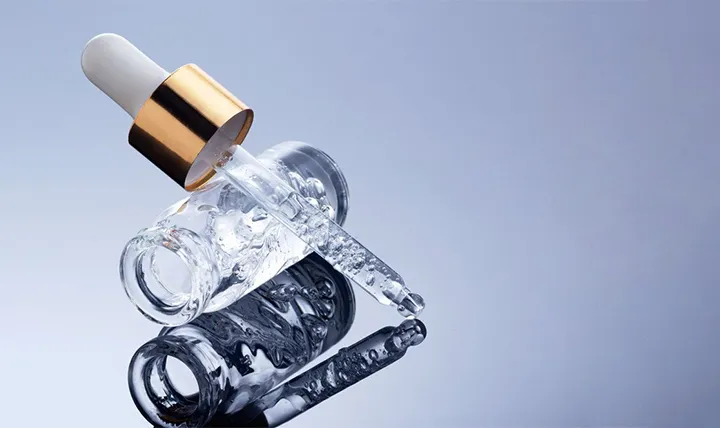A gold-capped serum dropper resting on a clear bottle with a gray background.