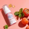 A bottle of Xiran Whole Body Deodorant Cream surrounded by mint leaves and persimmons on a peach background.