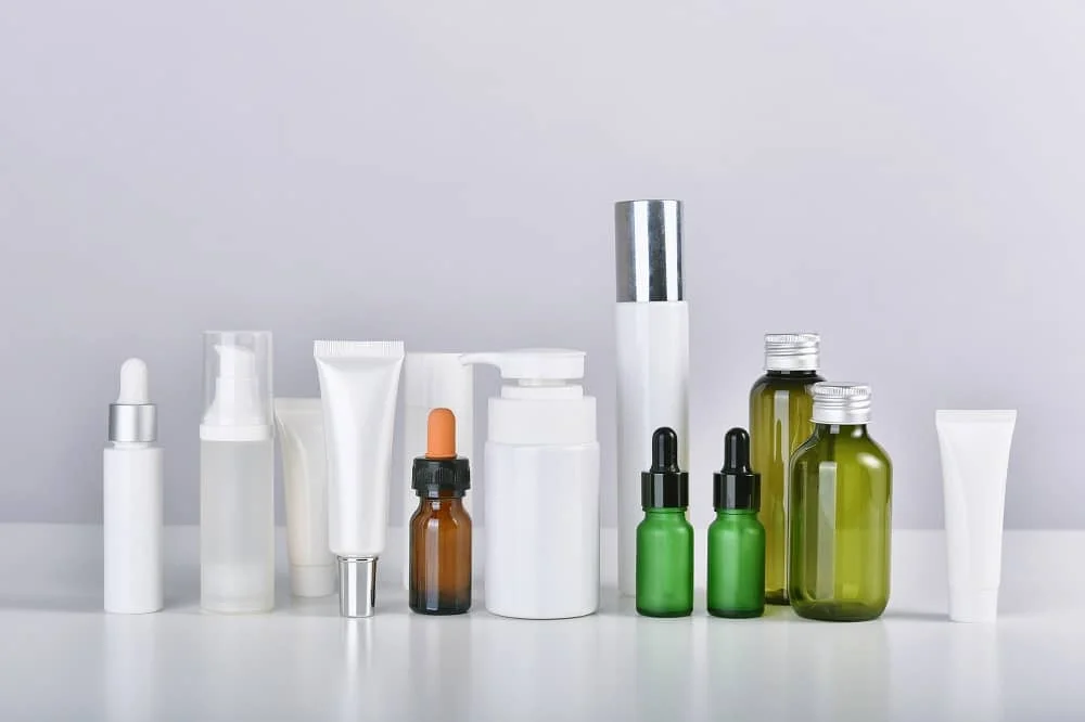A collection of assorted skincare bottles and tubes with varying designs, including droppers, pumps, and twist-off caps, on a neutral background.